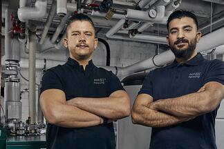Zwei Heizungs-Anlagenmechaniker der b&h concept AG stehen mit verschränkten Armen in Heizungskeller.